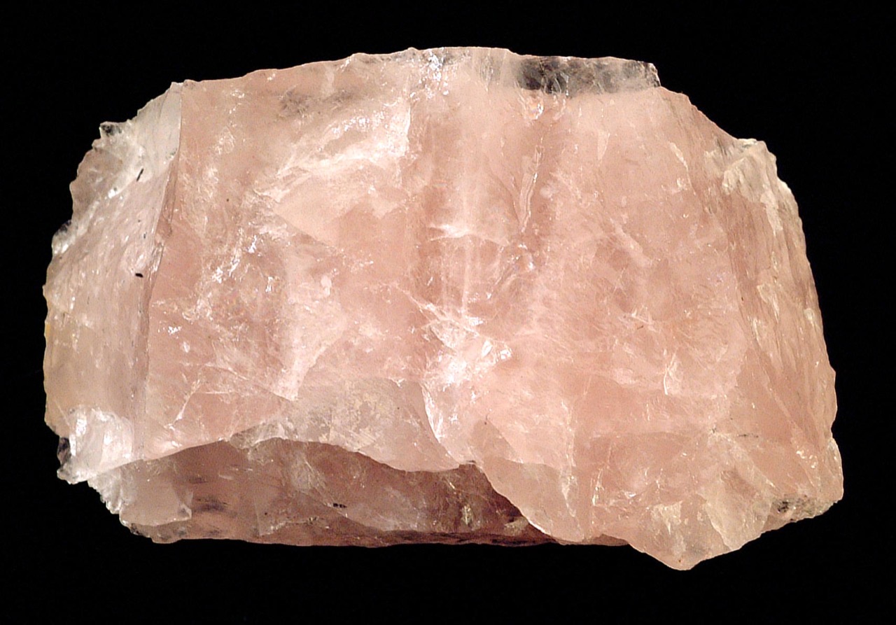 A rough, translucent rose quartz specimen in soft pink tones against a black background.