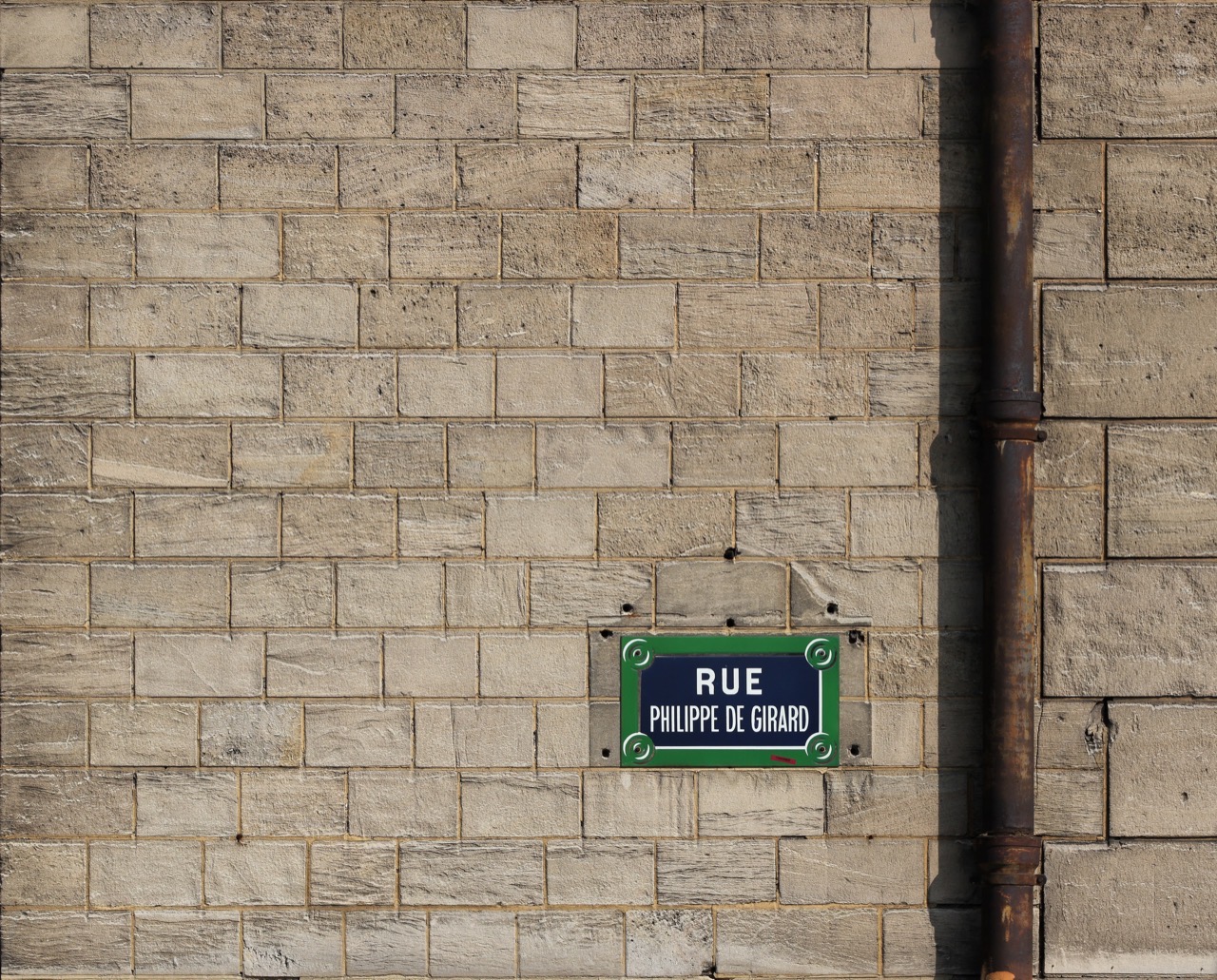 A pale cream limestone block wall with a green municipal street sign reading Rue Philippe de Girard.