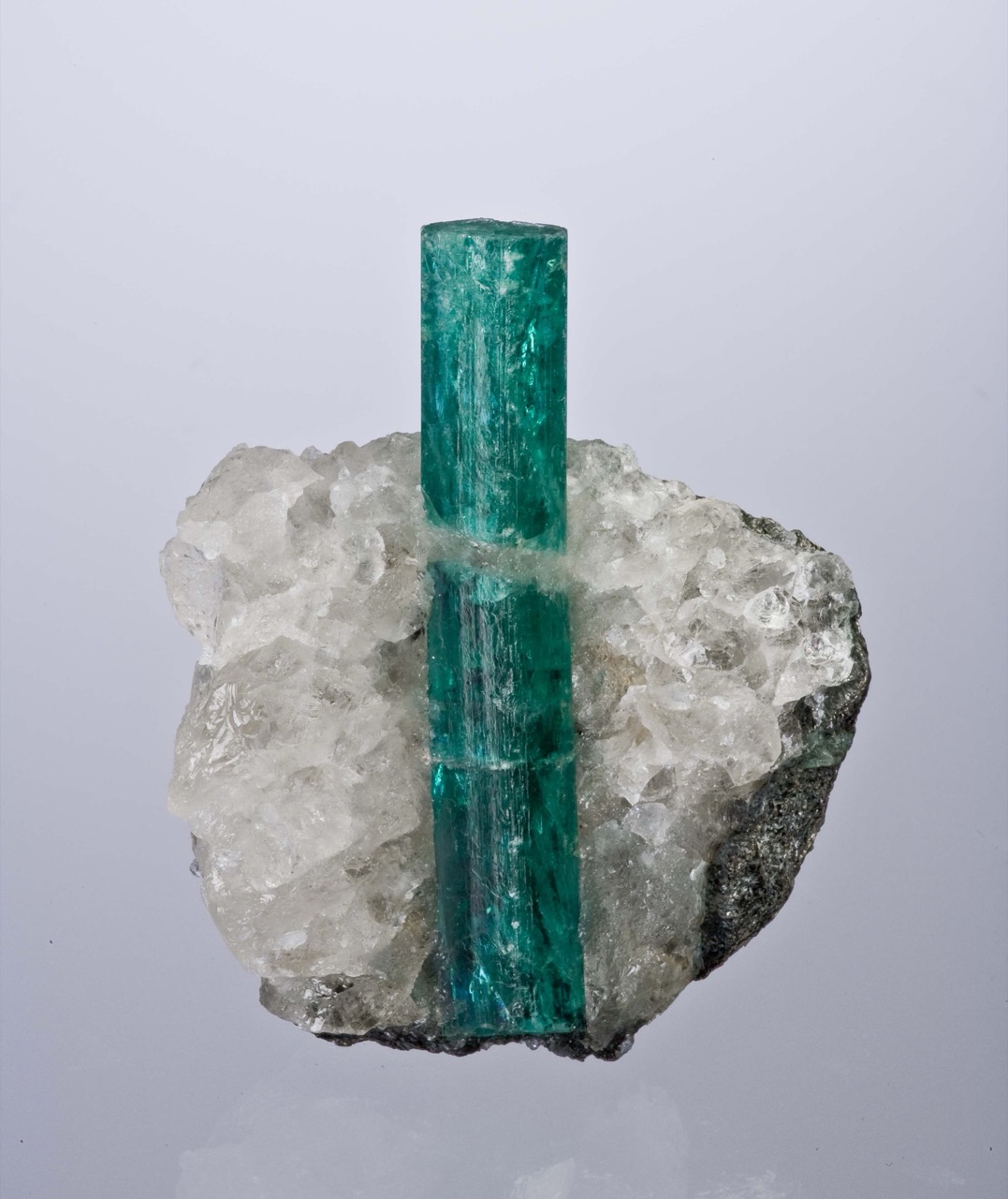 A vivid green emerald crystal embedded in white quartz matrix rock.