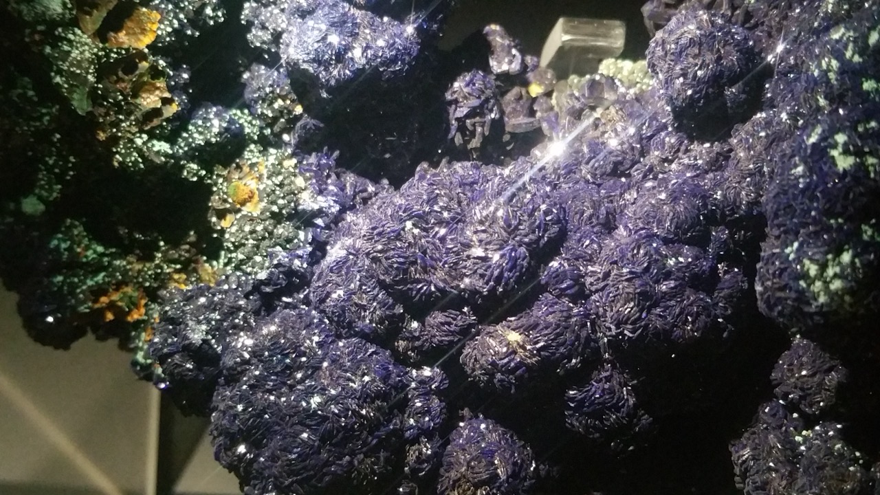 Sparkling deep blue-violet azurite crystal cluster, with small malachite and pyrite crystals nearby, displayed at the Natural History Museum, London.