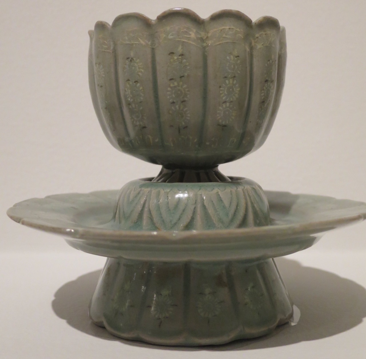 A pale sage-grey celadon ceramic cup and stand with carved floral decoration, from 12th-century Korea.