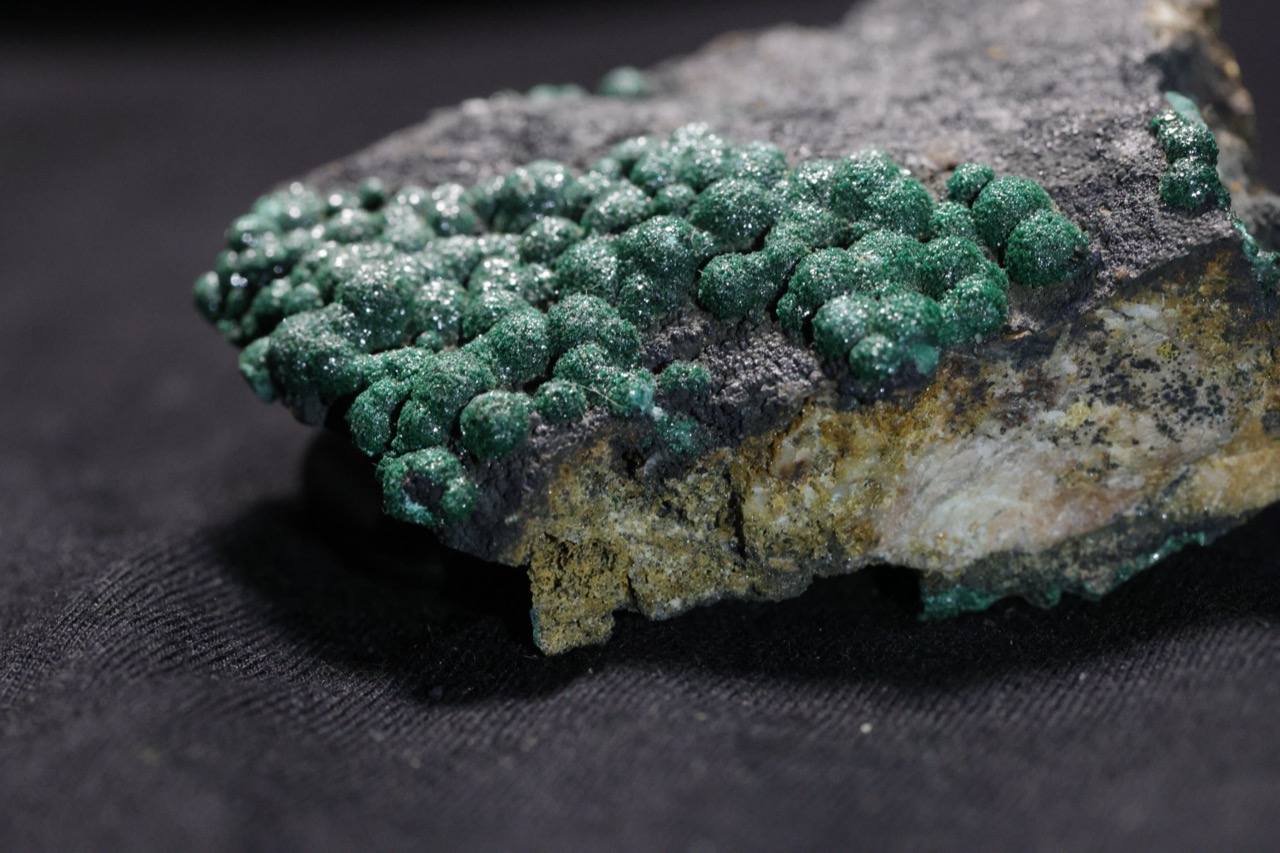 Close-up of botryoidal malachite, a mineral with rounded, grape-like green clusters, on host rock.