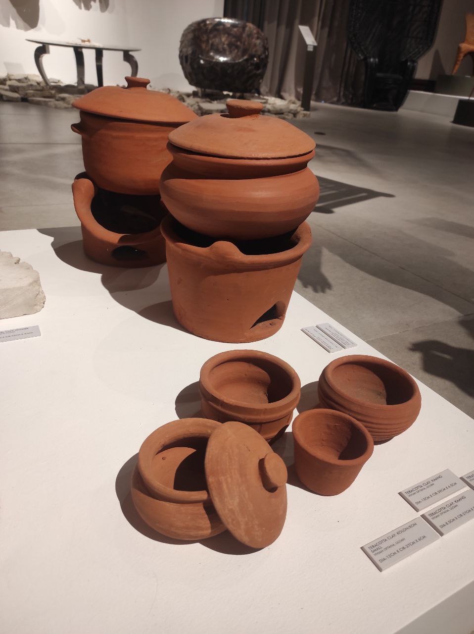 A display of unglazed terracotta clay cooking pots and lids of varying sizes.