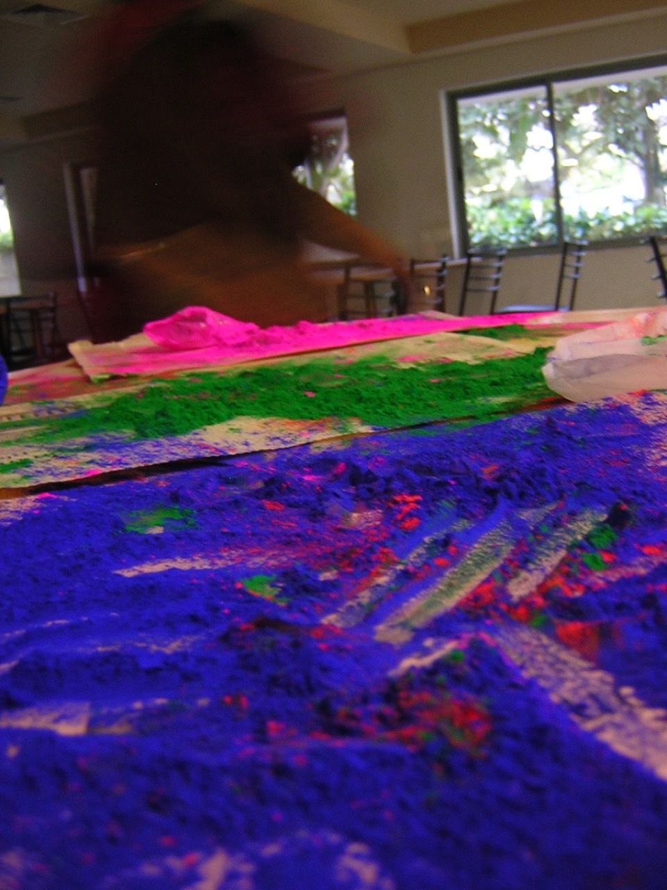 Close-up of vivid blue, pink and green Holi festival powders spread across a surface.
