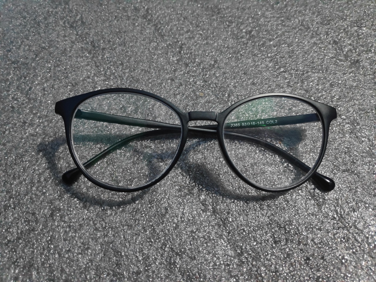 A pair of round black-frame glasses on a neutral speckled background.