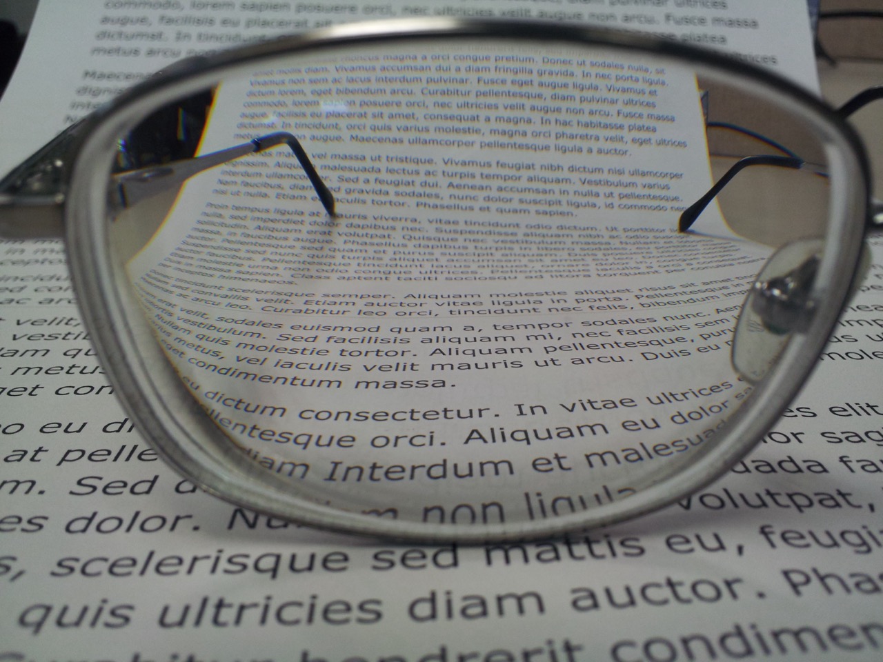 Thin metal-frame glasses held over a page of text, showing the lens's visible optical gradient.