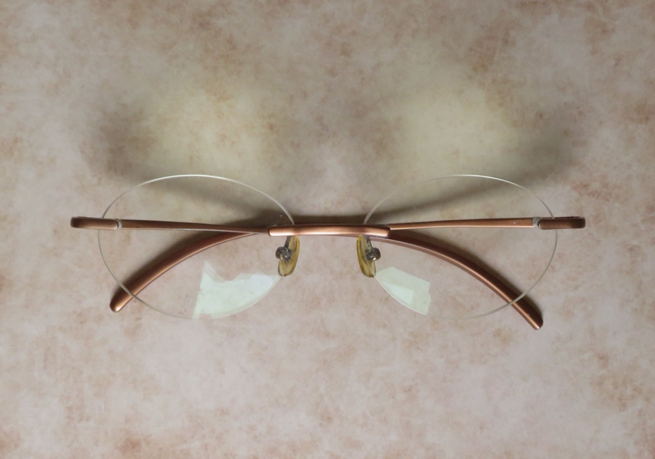 Rimless glasses with thin bronze-toned metal bridge and temple pieces, no surrounding frame around the lenses.