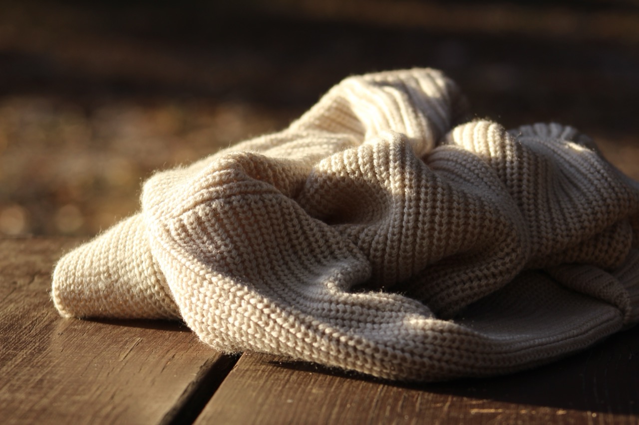 A cream knit sweater draped in soft folds on a dark wood surface, lit by warm evening light.