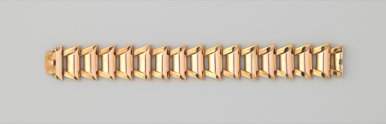 A hinged-link yellow gold bracelet with a clasp, photographed on a plain grey background.
