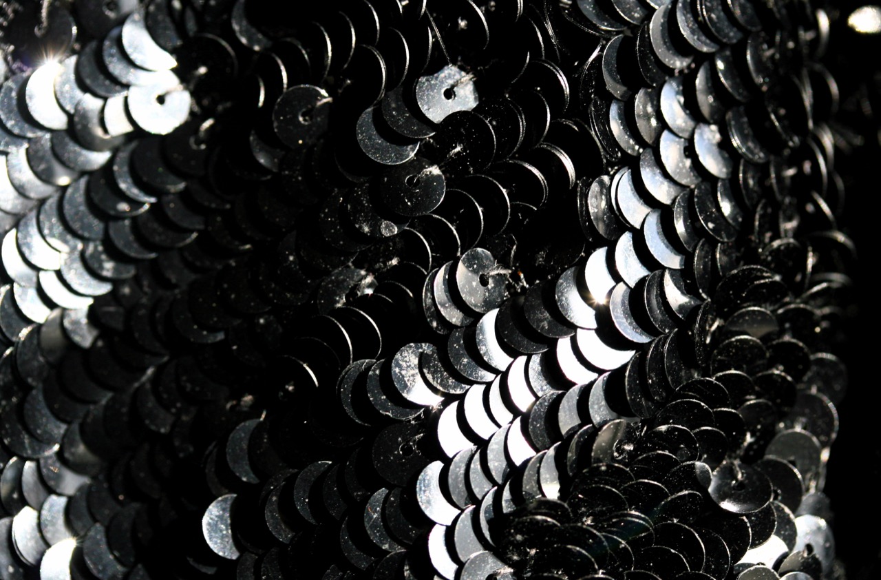 Macro close-up of overlapping dark silver sequins on fabric, catching light unevenly.