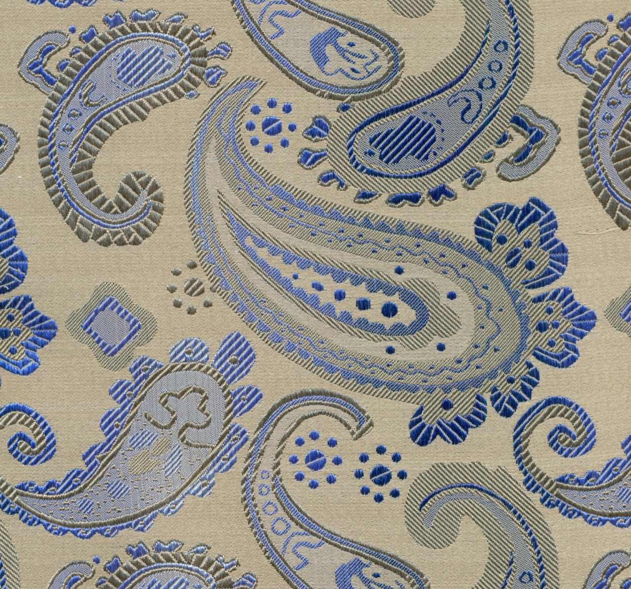 Close-up of a silk pocket square with a traditional blue-grey paisley pattern on a warm neutral ground.