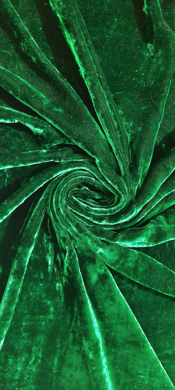 Close-up of deep green velvet fabric, gathered into a spiral fold showing its pile texture.