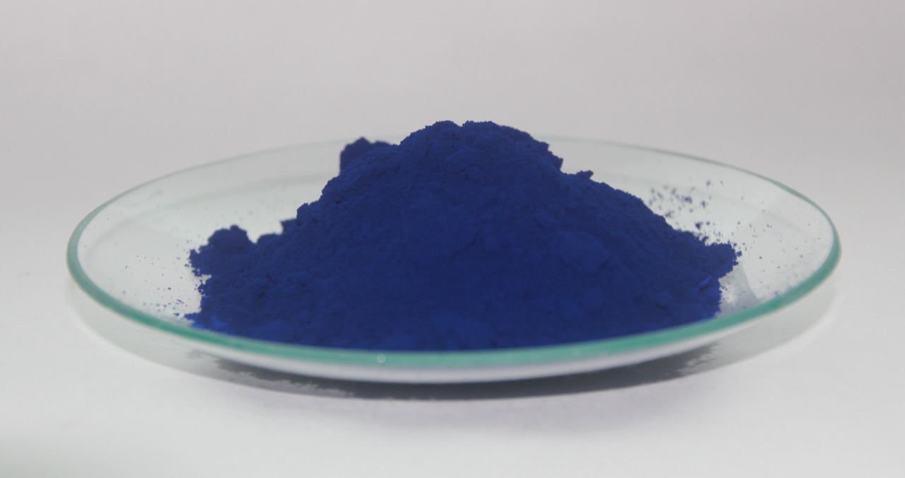 A mound of dark blue Prussian blue pigment powder on a glass dish.