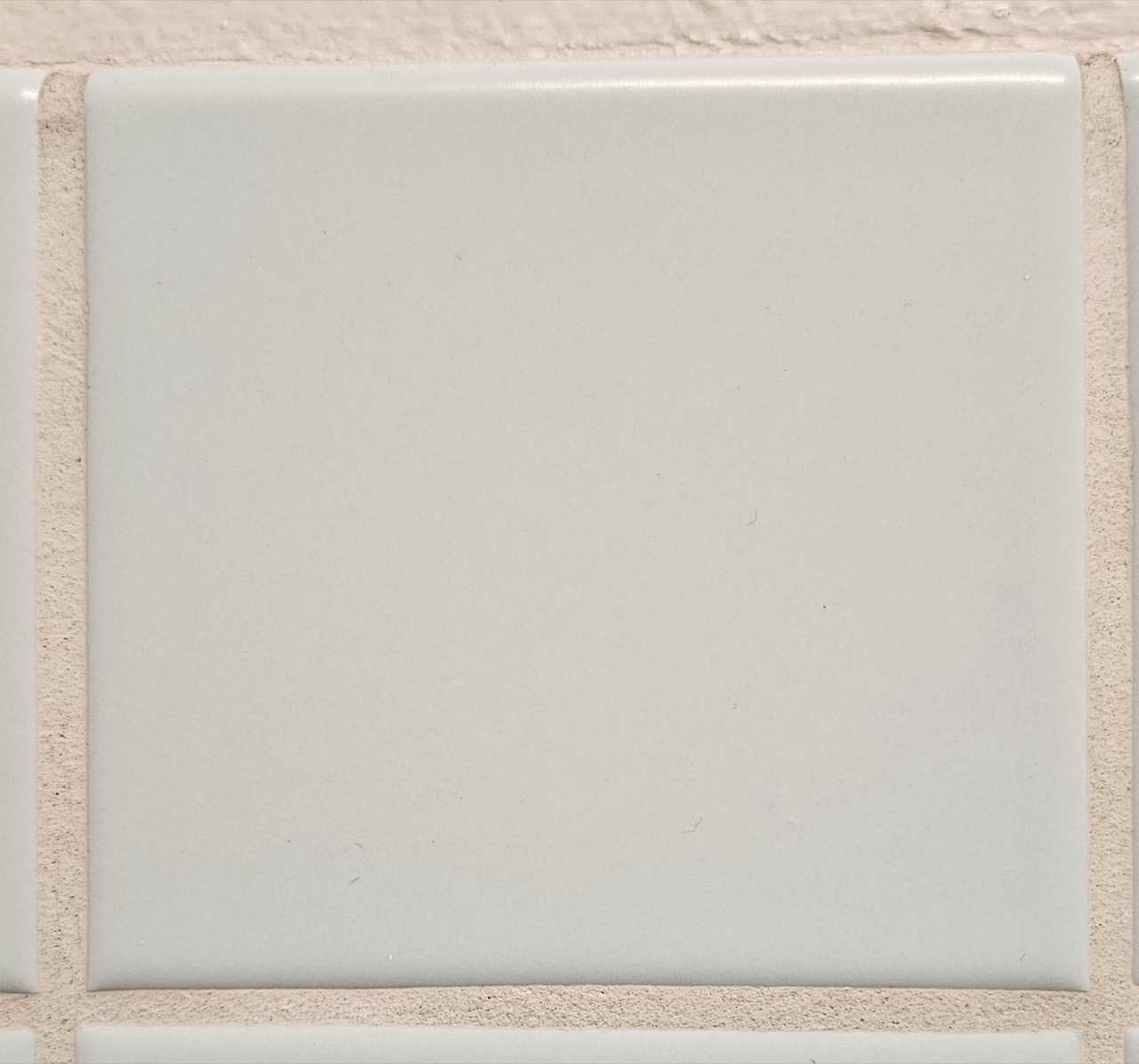 Close-up of a square pale blue-grey ceramic wall tile with visible grout lines.