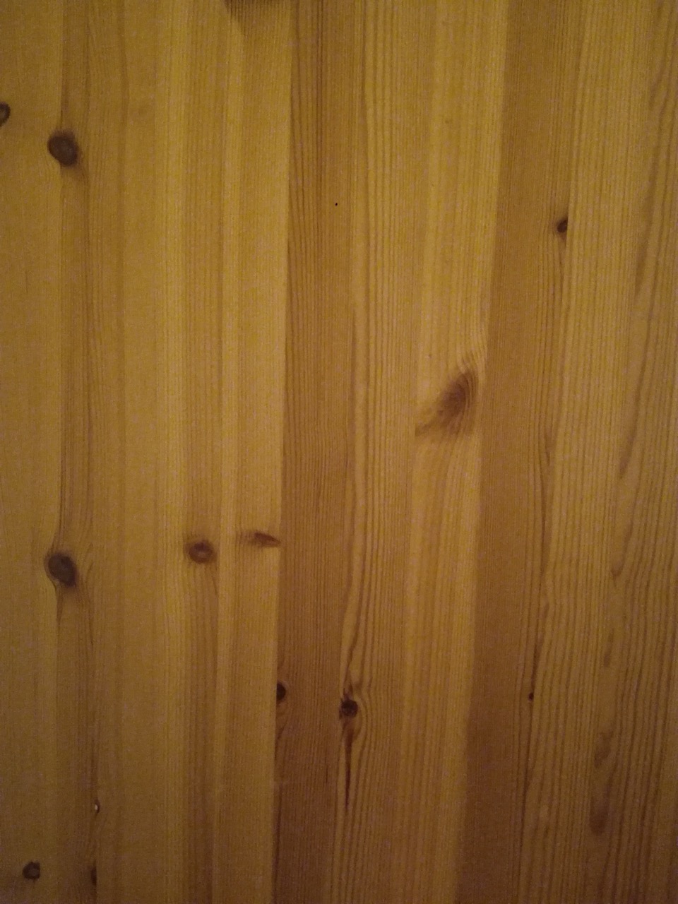 Close-up of knotty pine wood boards with a glossy lacquered finish, showing visible knots and grain.