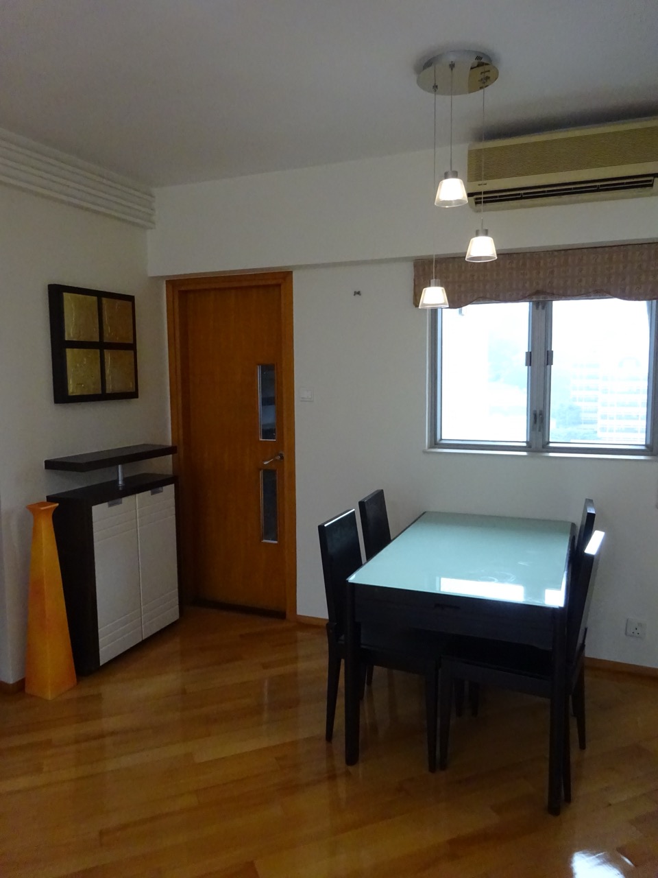 A combined dining and living room with a dining table, warm wood flooring and a large window.
