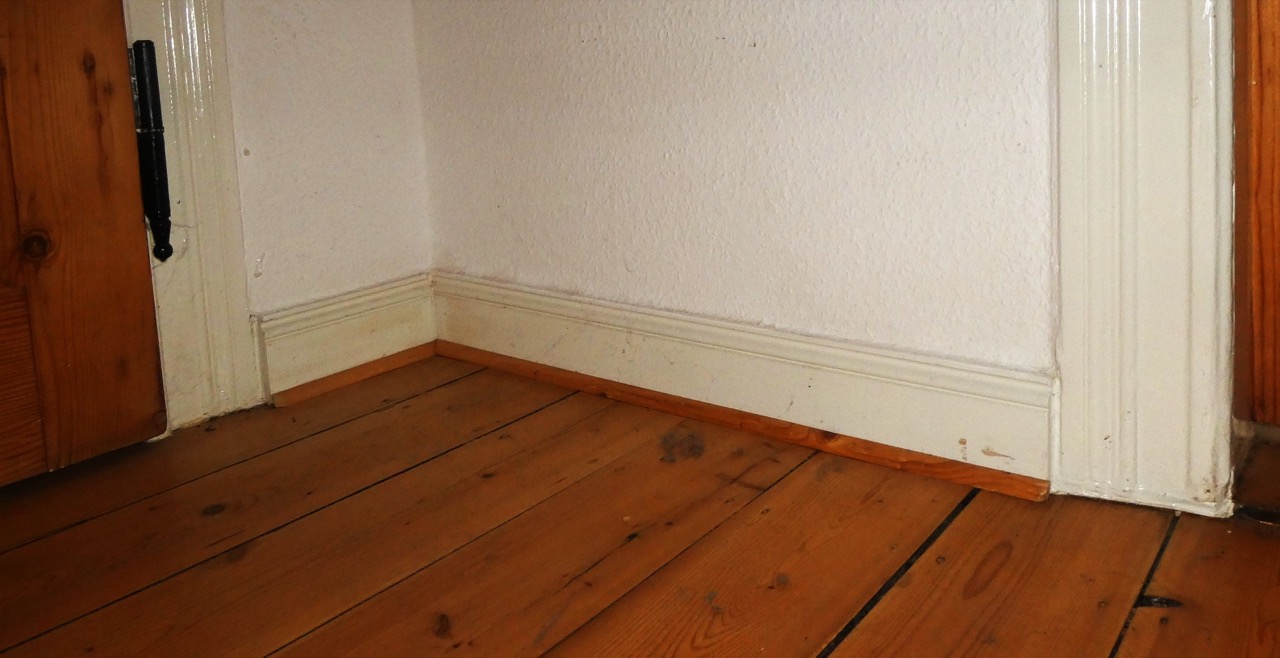 A painted off-white skirting board against a warm wood floor and matching pine door.