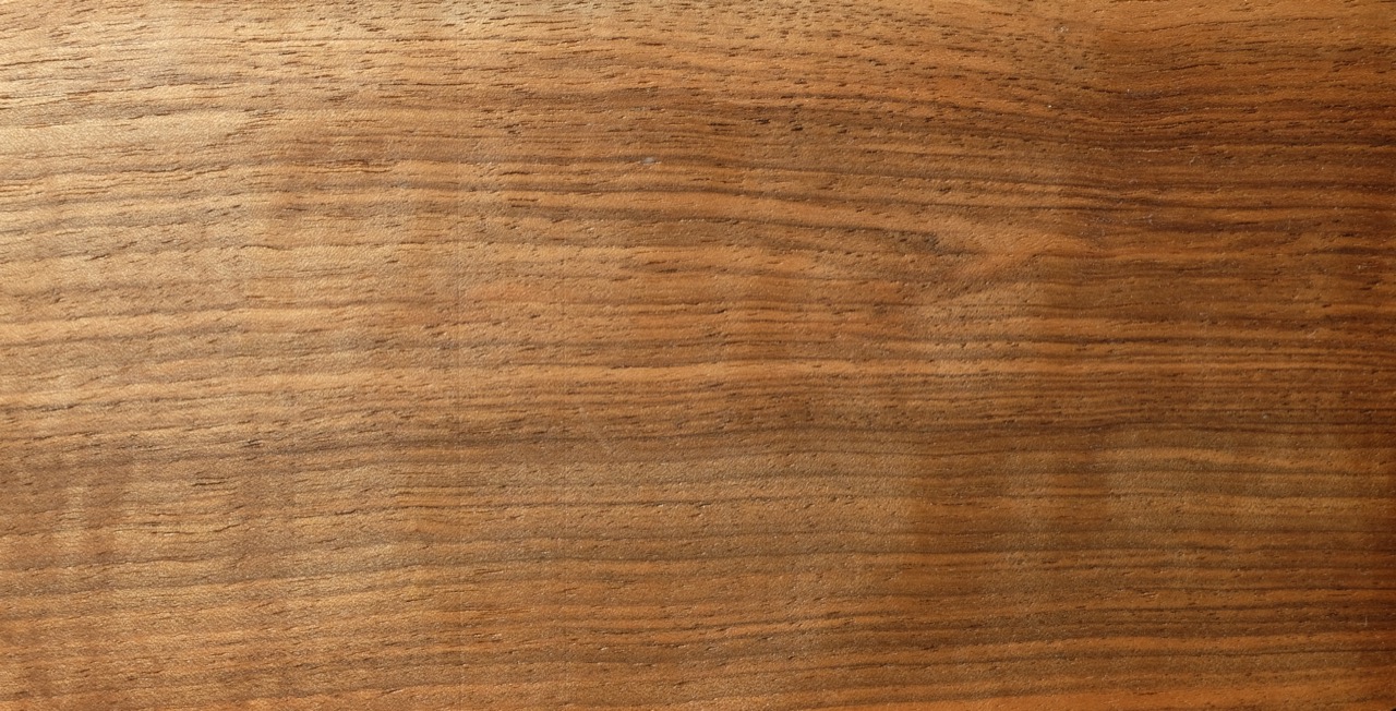 Close-up of walnut wood veneer showing fine, straight grain in warm mid-to-dark brown tones.