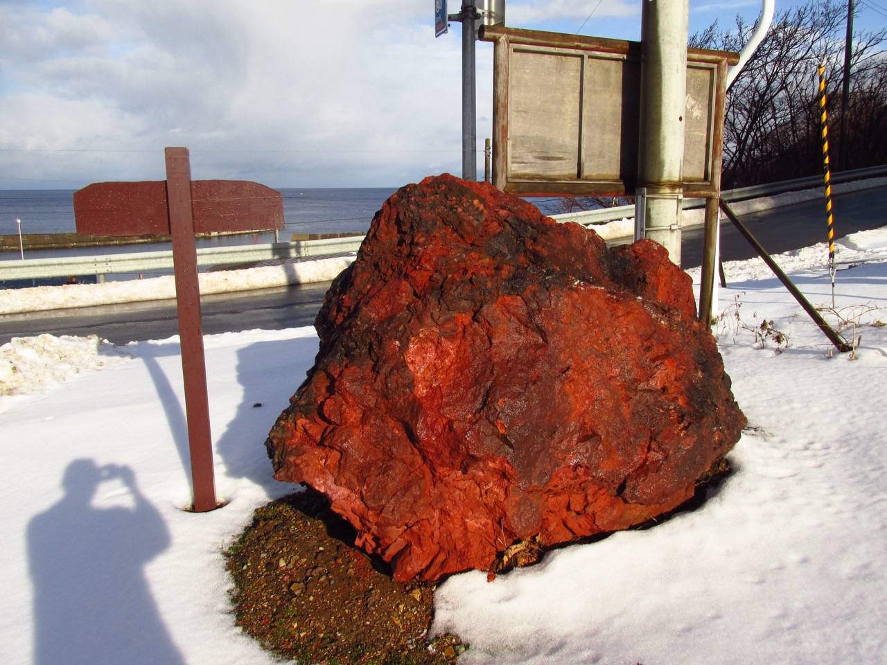 A large, deep red iron-oxide boulder, a protected natural monument in Aomori, Japan.