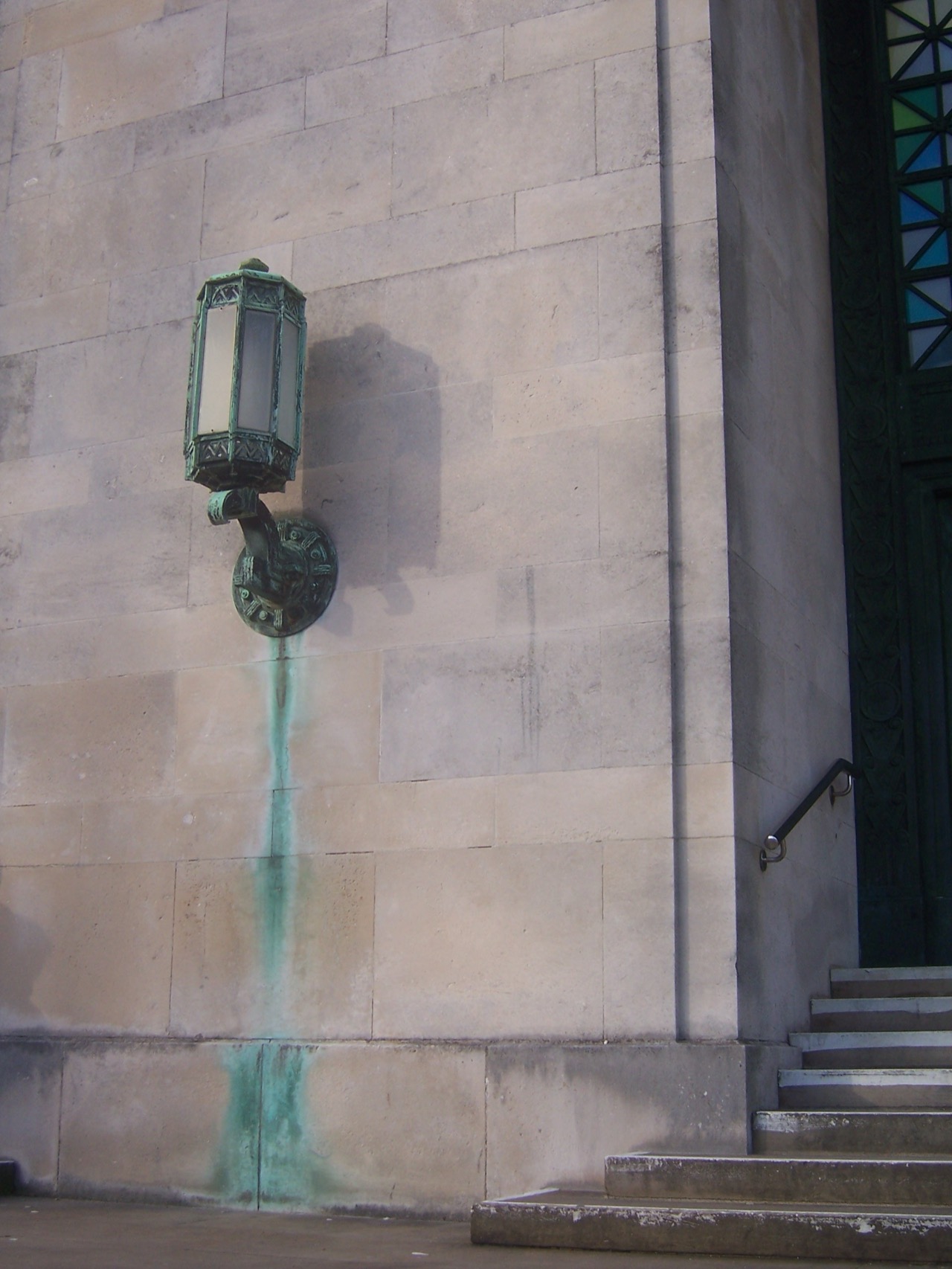 A streak of blue-green verdigris running down a pale stone wall from a corroded copper fixture.